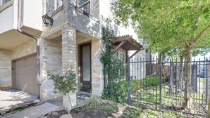 A residential building with a stone facade, a garage door, and a small garden area with a tree and a metal fence.
