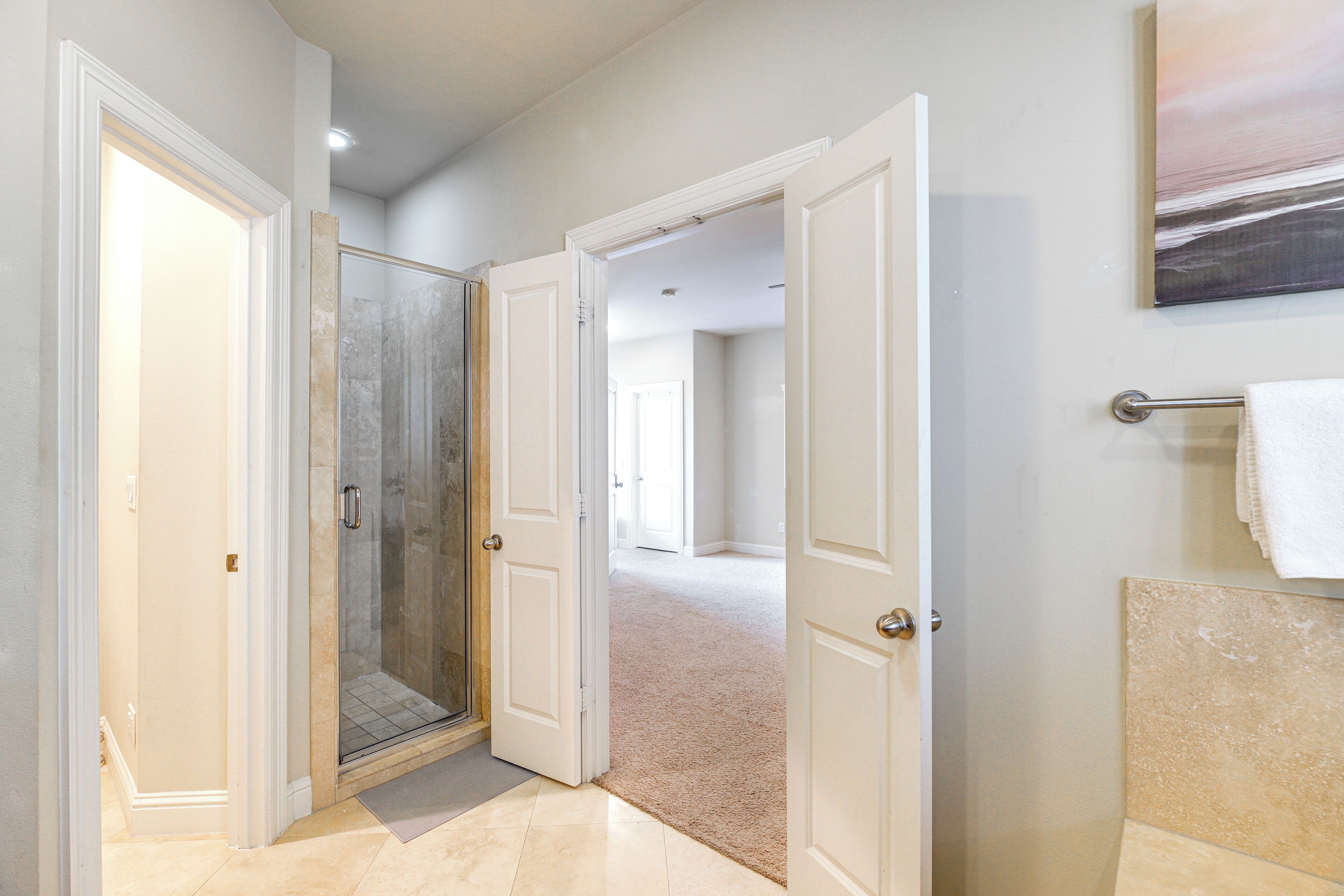A hallway with a glass shower door, a beige carpet, and a white tiled floor.