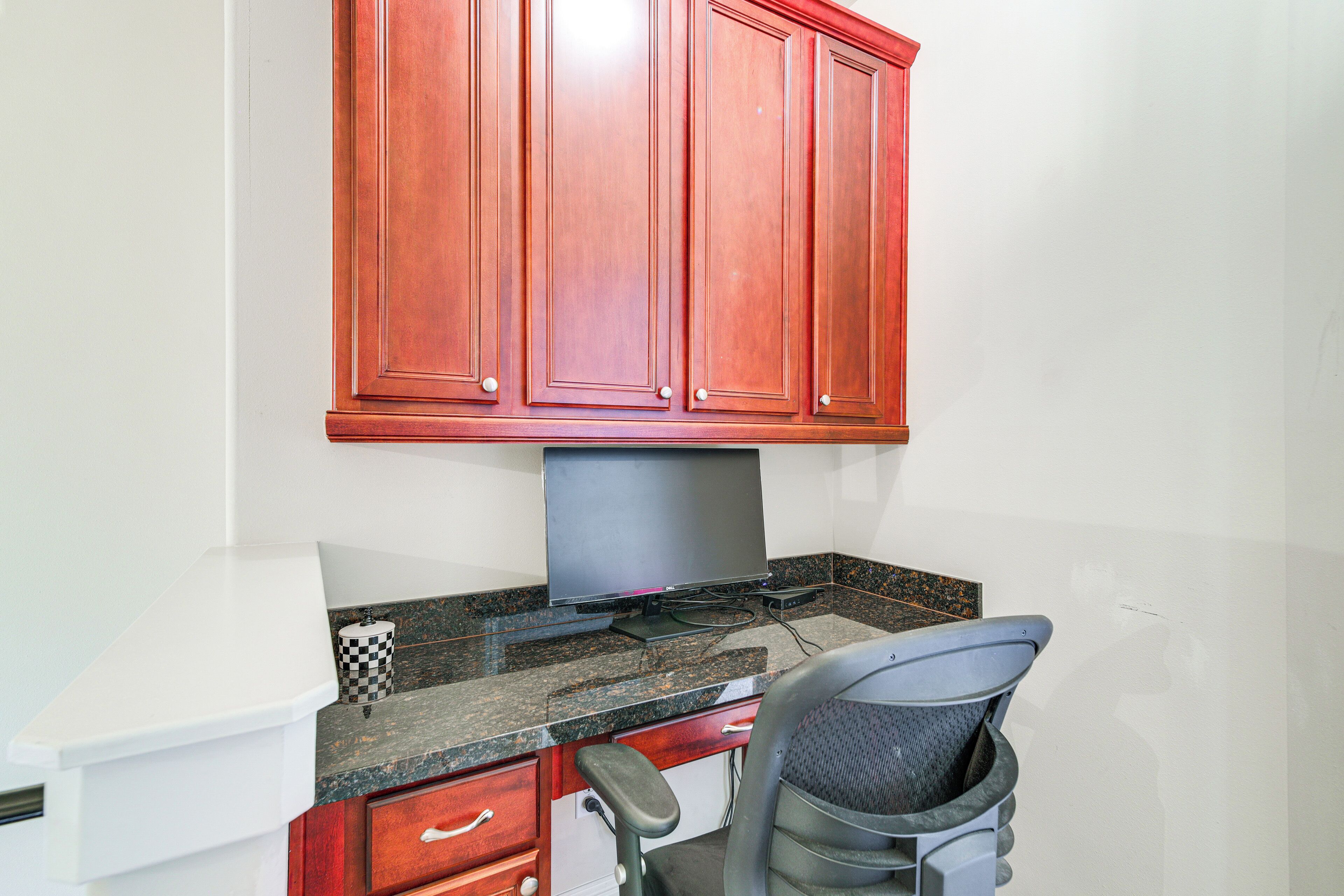 A kitchen with wooden cabinets, a granite countertop, a stove, and a chair.