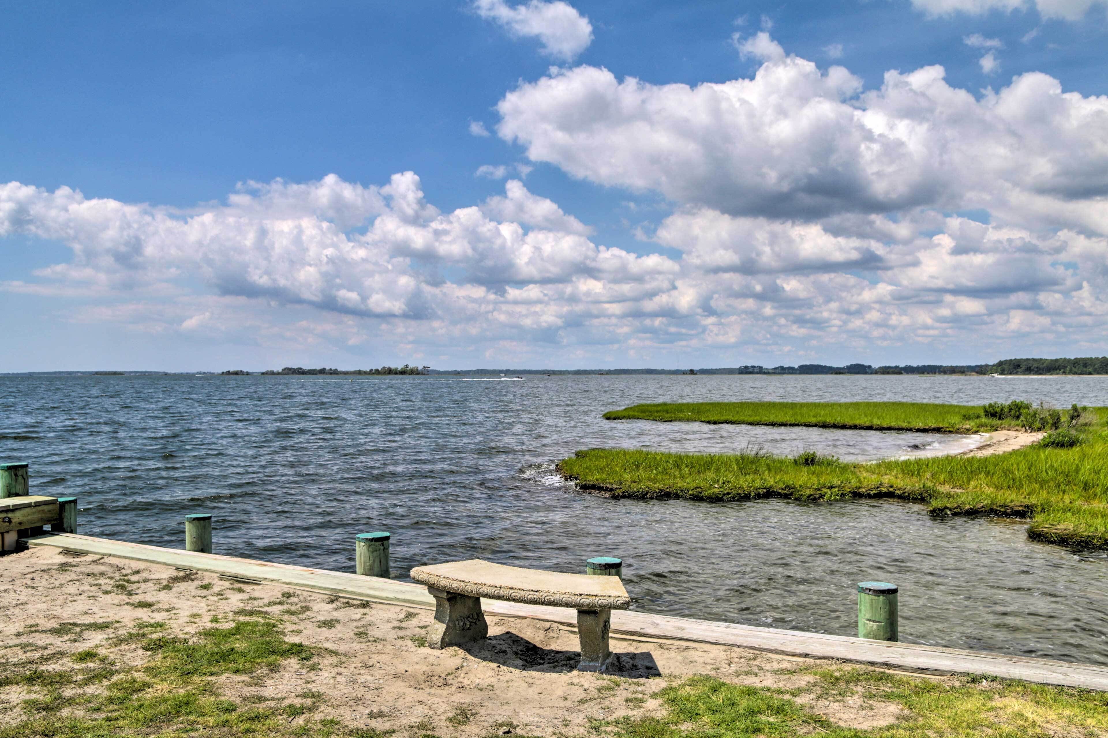 A waterfront park with a concrete bench, a wooden walkway, and grassy areas.