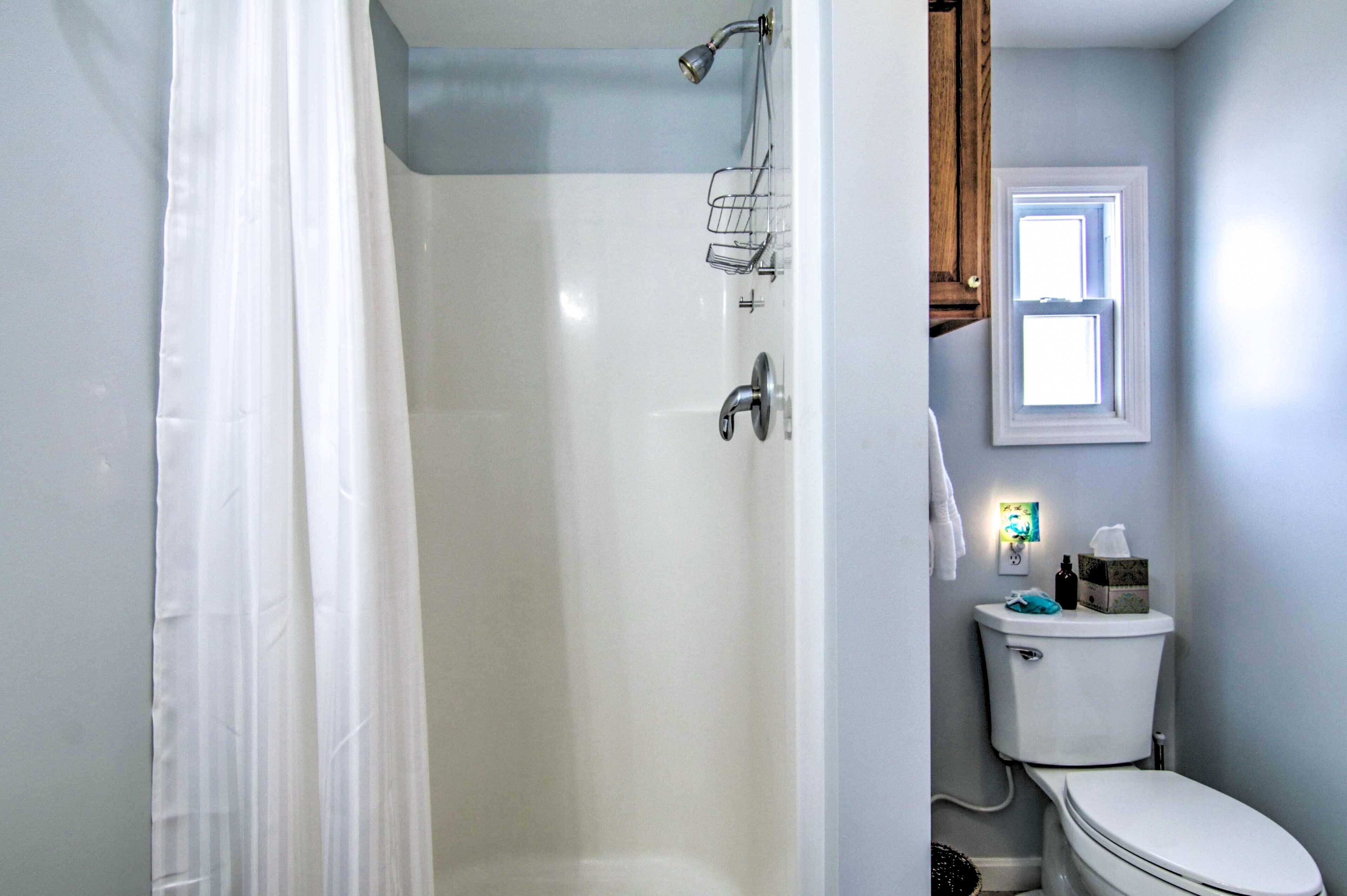 A bathroom with a shower, toilet, and a window.