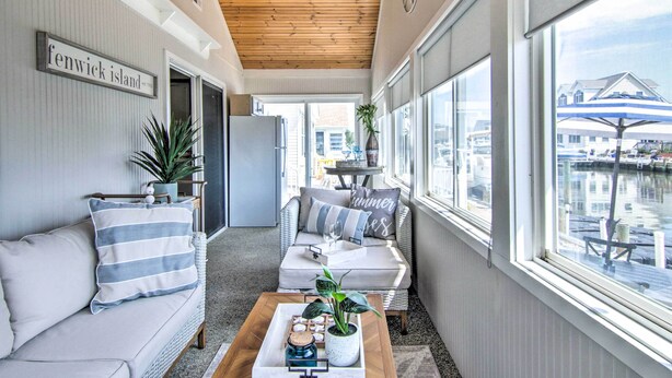 A cozy room with a sofa, a coffee table with a tray, and a view of the water outside. - Fire Pit + Views: Canal-front Fenwick Island Home (Selbyville)