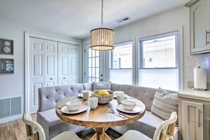 A dining area with a round wooden table, grey upholstered chairs, and a chandelier.