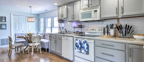 A modern kitchen with white cabinets, a microwave, and a dishwasher. There is a dining area with a table and chairs.