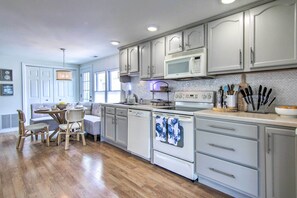 A modern kitchen with white cabinets, a microwave, and a dishwasher. There is a dining area with a table and chairs. - Fire Pit + Views: Canal-front Fenwick Island Home (Selbyville)