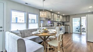 A modern kitchen with a dining area, featuring a sofa, dining table, chairs, and a chandelier. - Fire Pit + Views: Canal-front Fenwick Island Home (Selbyville)