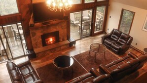 A spacious living room with a stone fireplace, leather sofas, and a large window overlooking a deck. - Lake Harmony Vacation Rental w/ Hot Tub & Views! (Lake Harmony)