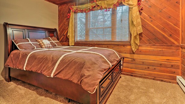 A wooden-paneled bedroom with a bed, a ceiling fan, and a window with curtains. - Lake Harmony Vacation Rental w/ Hot Tub & Views! (Lake Harmony)