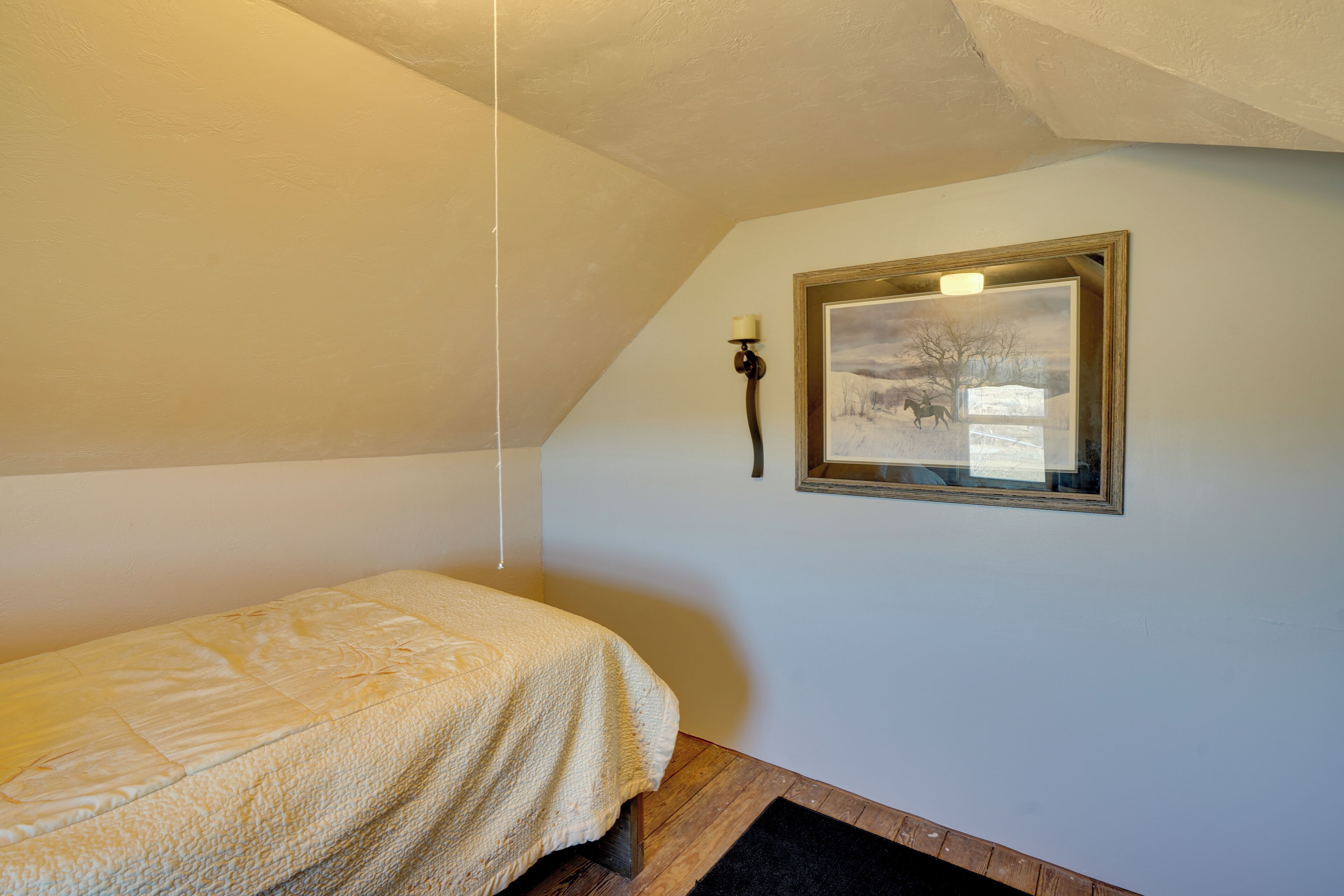 A bedroom with a single bed, a framed picture on the wall, and a hanging lamp.