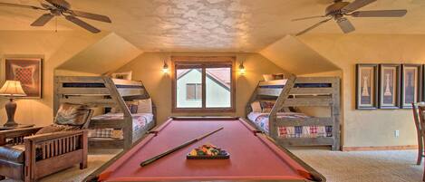 A cozy attic room with a pool table, bunk beds, ceiling fans, and framed artwork.