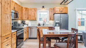 A kitchen with wooden cabinets, stainless steel appliances, a dining table with chairs, and a window. - Game Room & Wraparound Decks: Cullowhee Home! (Cullowhee)