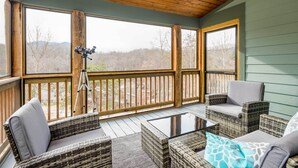 A covered outdoor area with wicker furniture, a tripod, and a view of the outdoors. - Game Room & Wraparound Decks: Cullowhee Home! (Cullowhee)