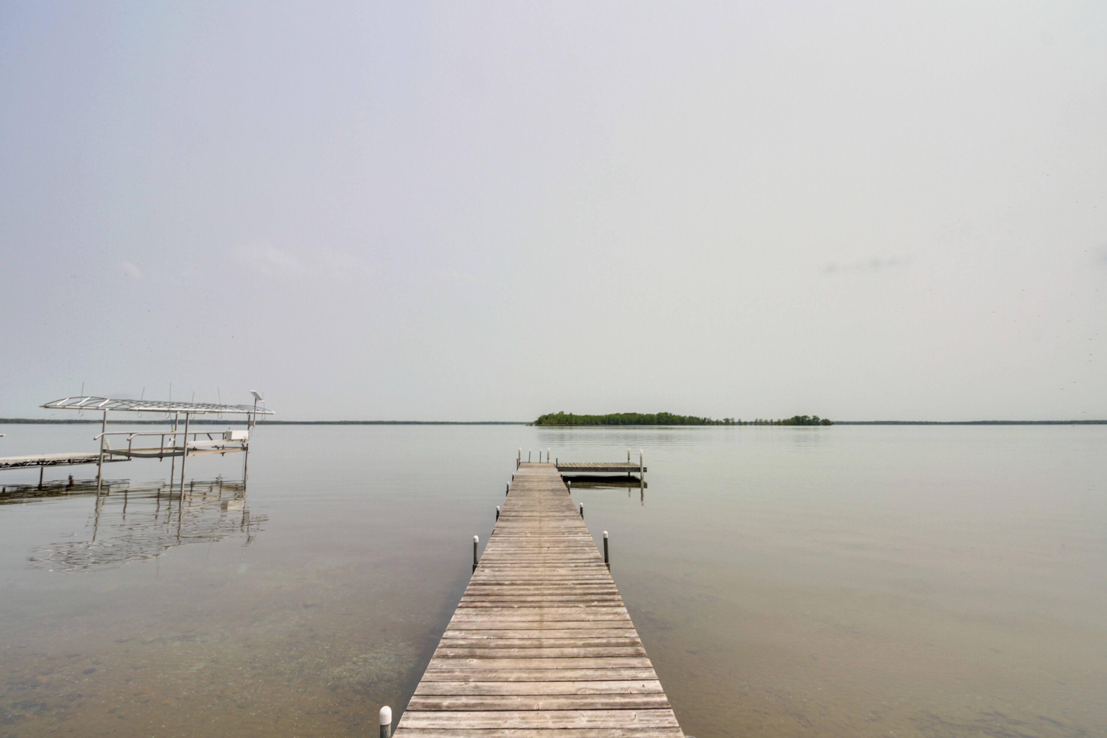 Un muelle de madera que se extiende sobre aguas tranquilas, con una pequeña isla a lo lejos.