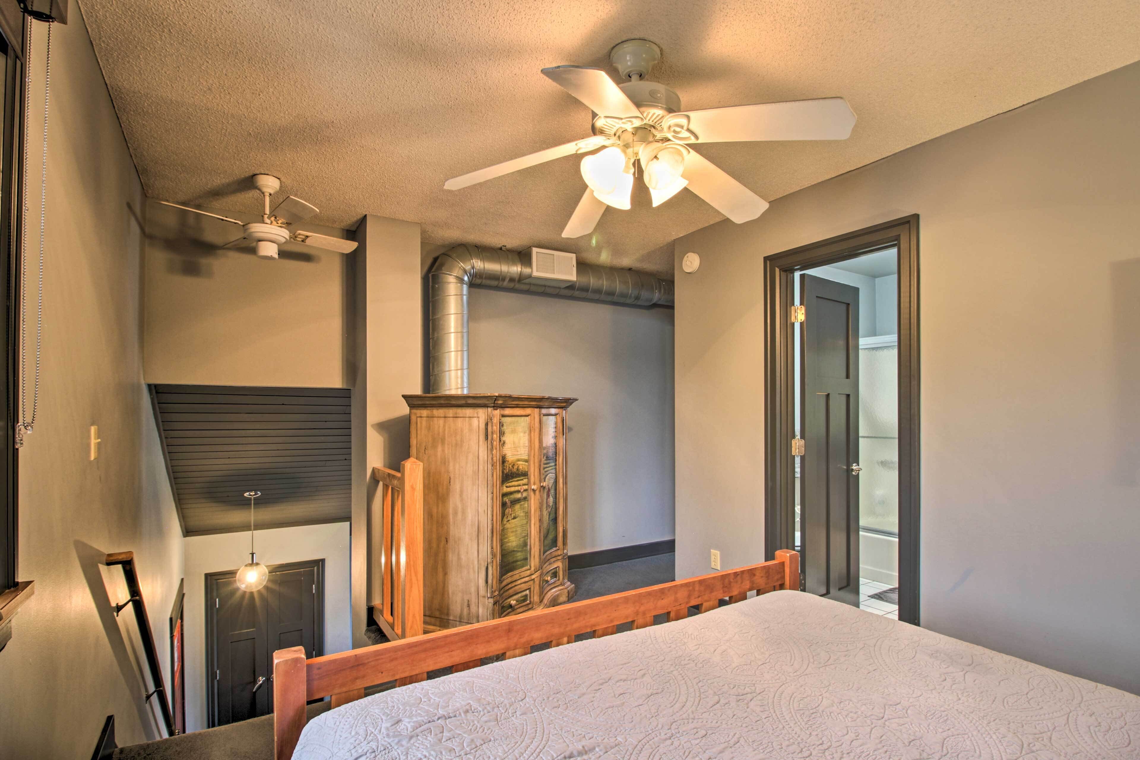 A bedroom with a wooden bed frame, a ceiling fan, a wardrobe, and a visible ductwork.
