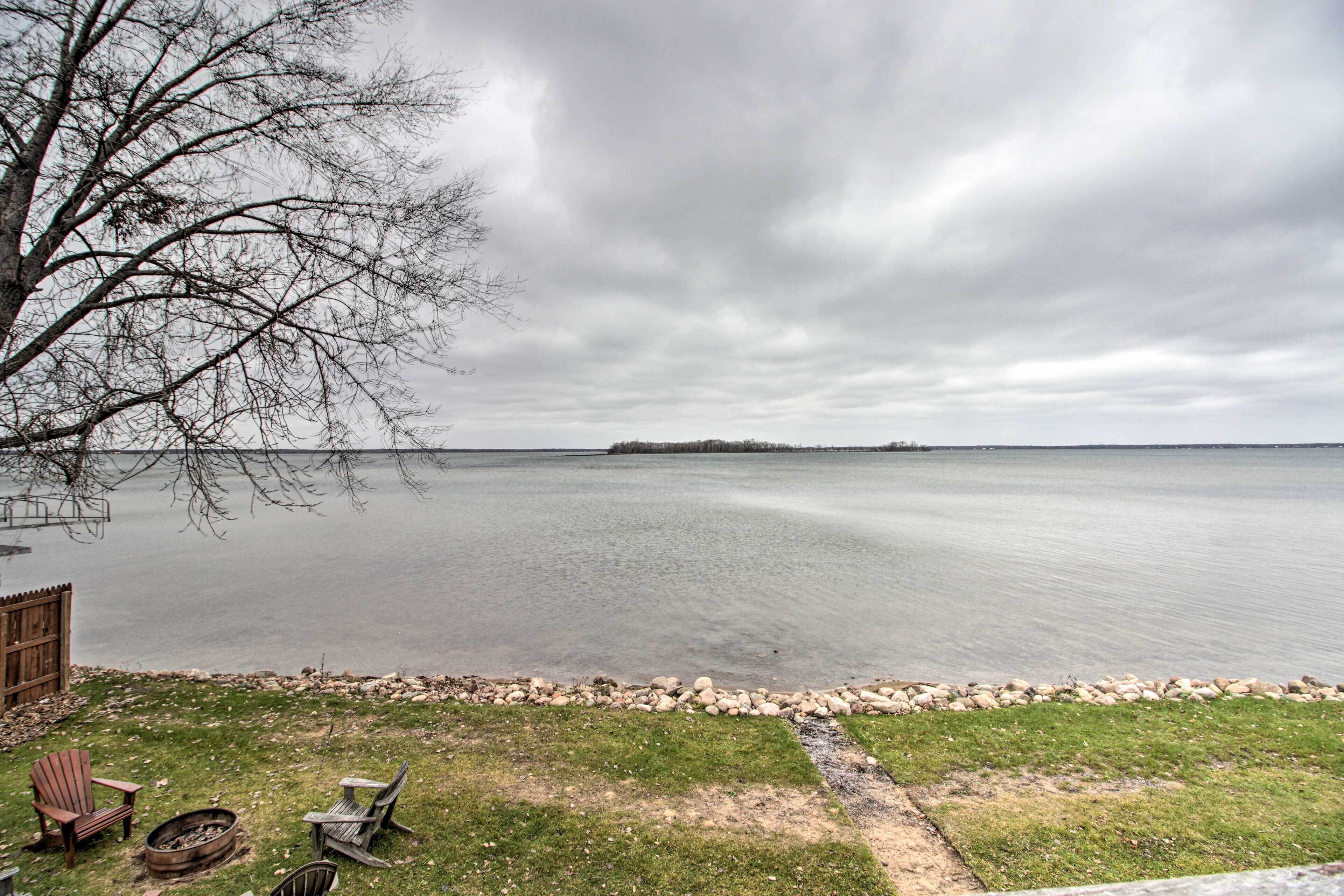 A lakeside view with a wooden deck, a fire pit, and outdoor seating.