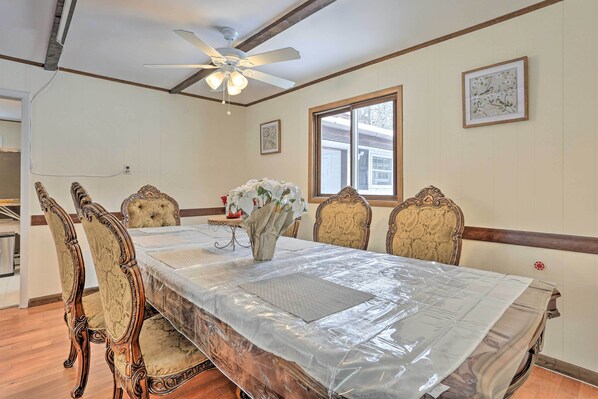 A dining room with a large table covered by a plastic sheet, surrounded by ornate chairs.