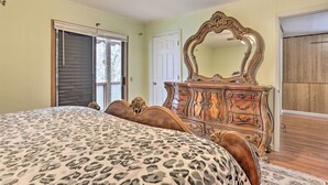 A bedroom with a large bed, a wooden dresser, a mirror, and a door leading to a balcony. - Large Greeley House w/ 2 Game Rooms + Yard! (Greeley)