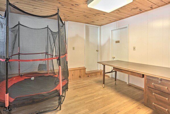 Een kamer met een houten vloer, een bureau met lades, een deur en een trampoline met veiligheidsnet.