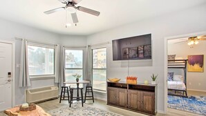 Una sala moderna con comedor, un ventanal grande, un ventilador de techo y una litera en la habitación contigua.