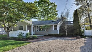 A single-story house with a front porch, a gravel driveway, and a white picket fence. - Luxury Hamptons Home on Canal w/ Dock & Kayaks! (East Quogue)
