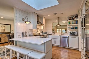 A modern kitchen with a central island, white cabinetry, stainless steel appliances, and a skylight. - Luxury Hamptons Home on Canal w/ Dock & Kayaks! (East Quogue)