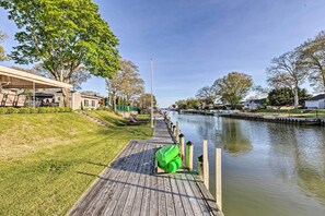 A wooden dock extending over a calm waterway, with a green kayak and a covered seating area on the left. - Luxury Hamptons Home on Canal w/ Dock & Kayaks! (East Quogue)