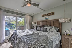 Un dormitorio con una cama grande, un ventilador de techo, un cabecero de madera y vistas a un área exterior por una puerta corrediza de vidrio.