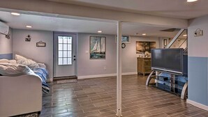 A living room with a sofa, a flat-screen TV, and a staircase leading to another level. - Luxury Hamptons Home on Canal w/ Dock & Kayaks! (East Quogue)