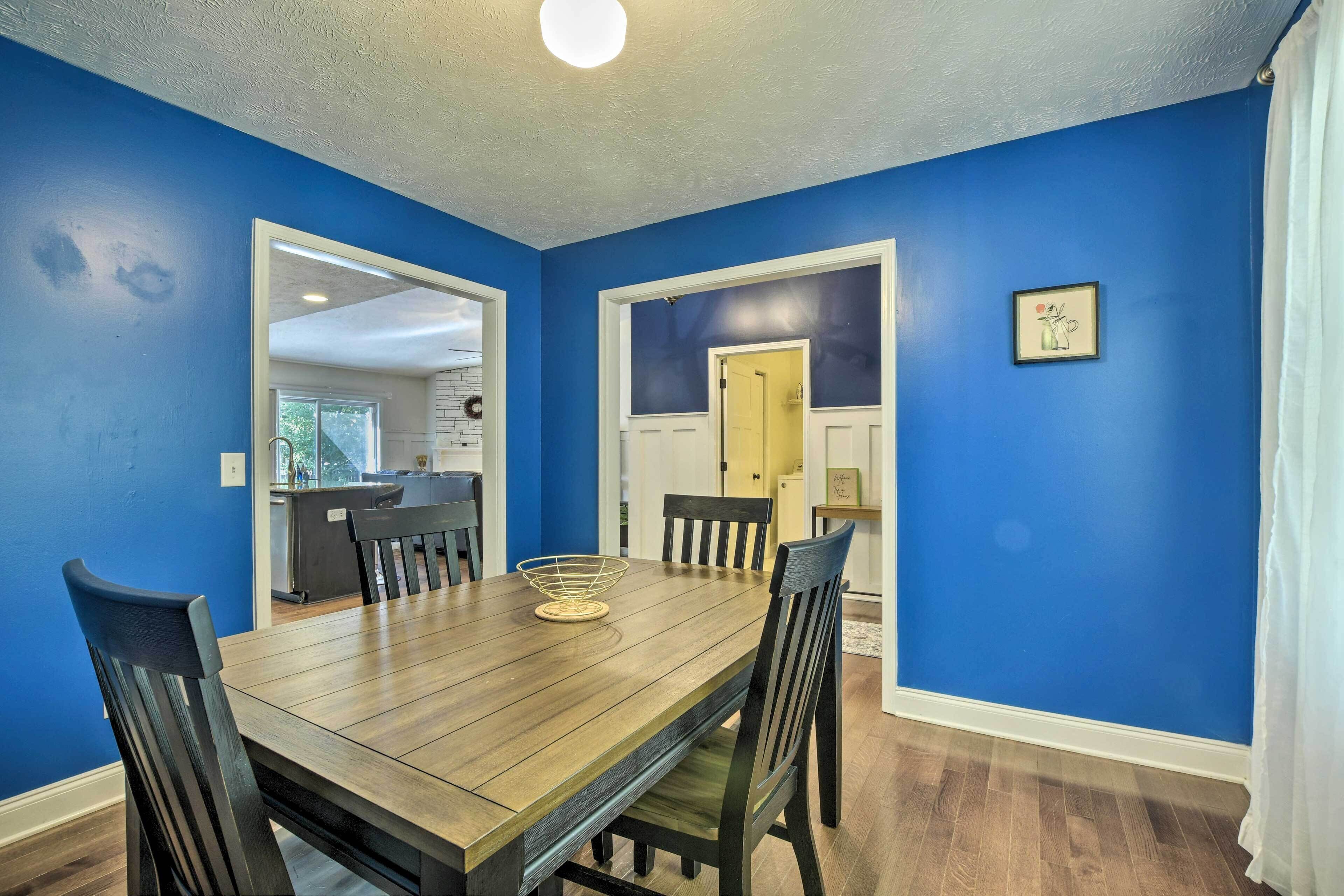 A dining area with a wooden table and chairs, blue walls, and a door leading to another room.