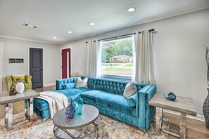 A modern living room with a teal sofa, a round coffee table, and a view of a house through a large window.