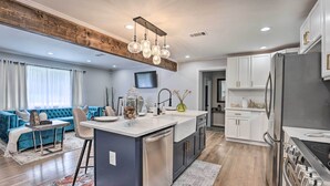 A modern kitchen with a central island, stainless steel appliances, and a dining area with a blue sofa and a small table. - Modern, Colorful Home ~ 2 Mi to Tuskegee Uni (Tuskegee)