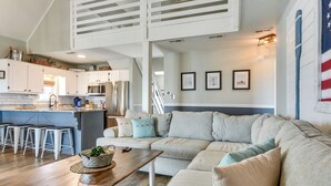 A modern kitchen with white cabinets, a dining area with a wooden table, and a living room with a beige sectional sofa. - Gorgeous OIB Escape w/ Dock & Canal View! (Ocean Isle Beach)
