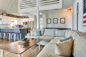 Una cocina moderna con armarios blancos, un comedor con mesa de madera y una sala de estar con sofá seccional color beige.
