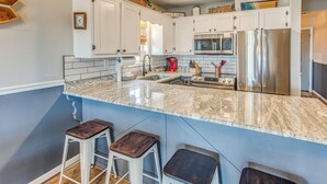 A kitchen with white cabinets, a stainless steel refrigerator, a microwave, and a coffee maker. There are two wooden stools and a sink with a faucet. - Gorgeous OIB Escape w/ Dock & Canal View! (Ocean Isle Beach)
