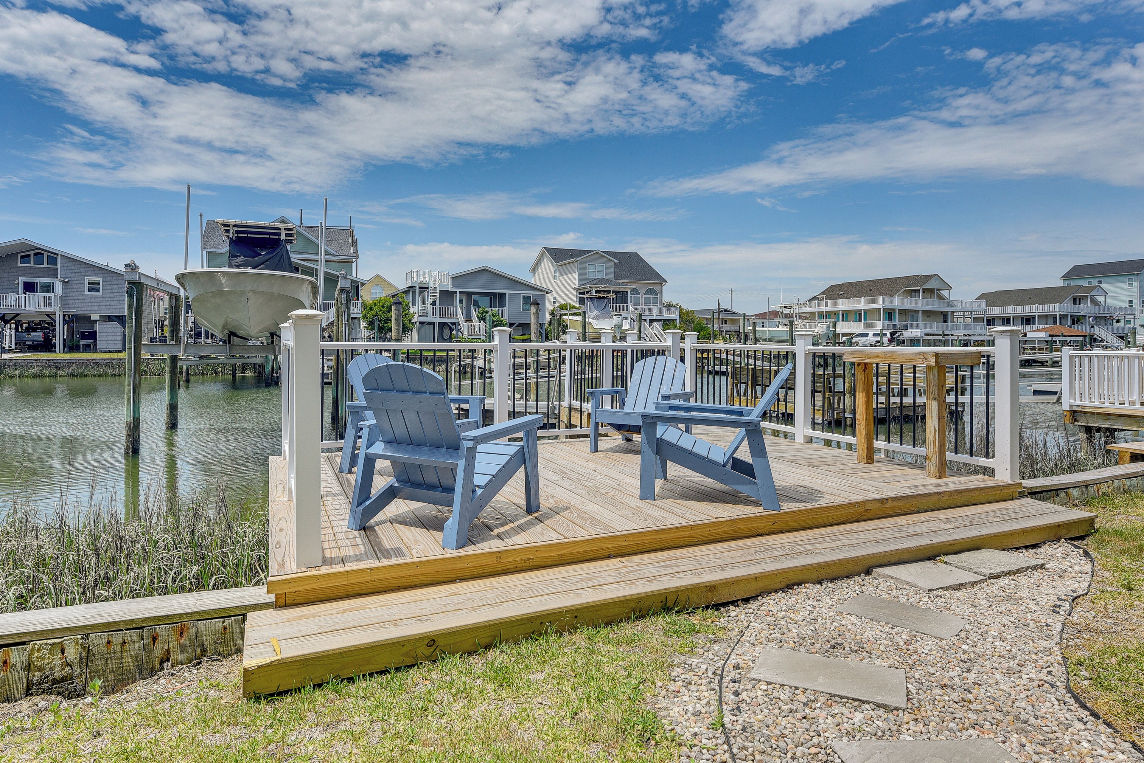 Een houten terras met stoelen, een boot en huizen aan het water.