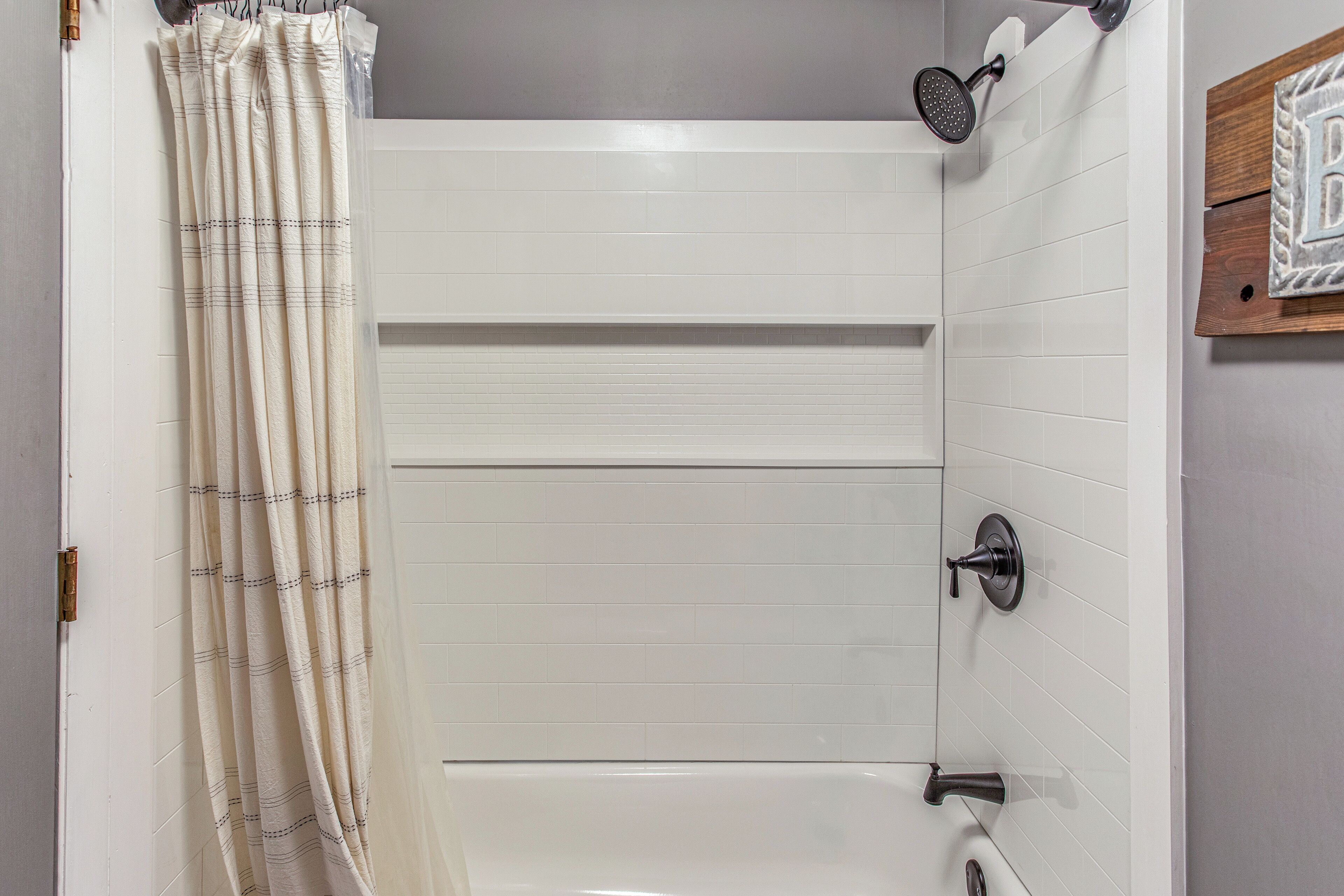 A bathroom with white tiled walls, a shower with a handheld showerhead, and a towel rack with a striped towel.