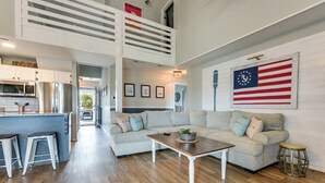 A spacious living area with a high ceiling, a kitchen with modern appliances, and a large American flag decoration. - Gorgeous OIB Escape w/ Dock & Canal View! (Ocean Isle Beach)