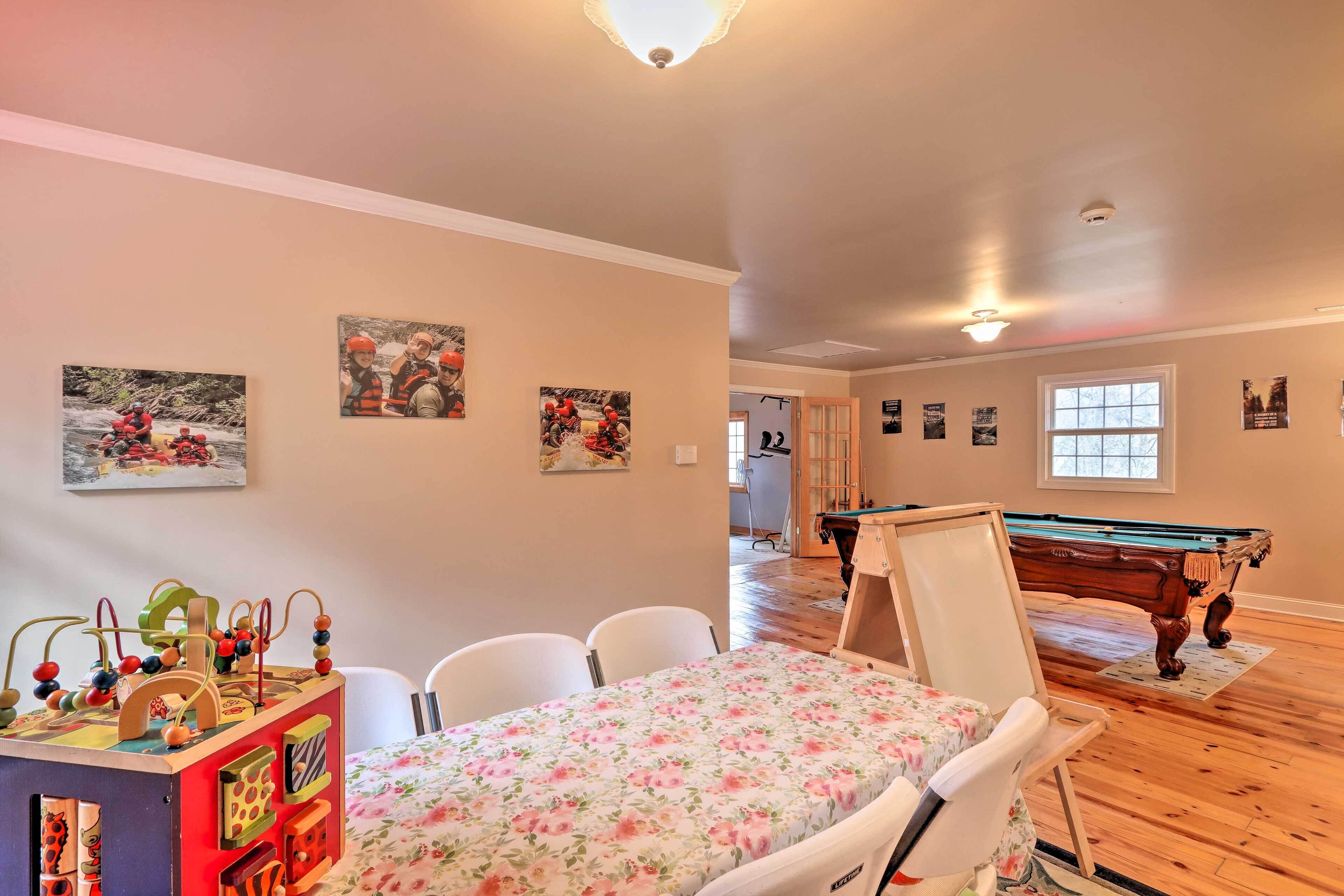 A room with a pool table, a dining table with chairs, and a colorful children's play area.
