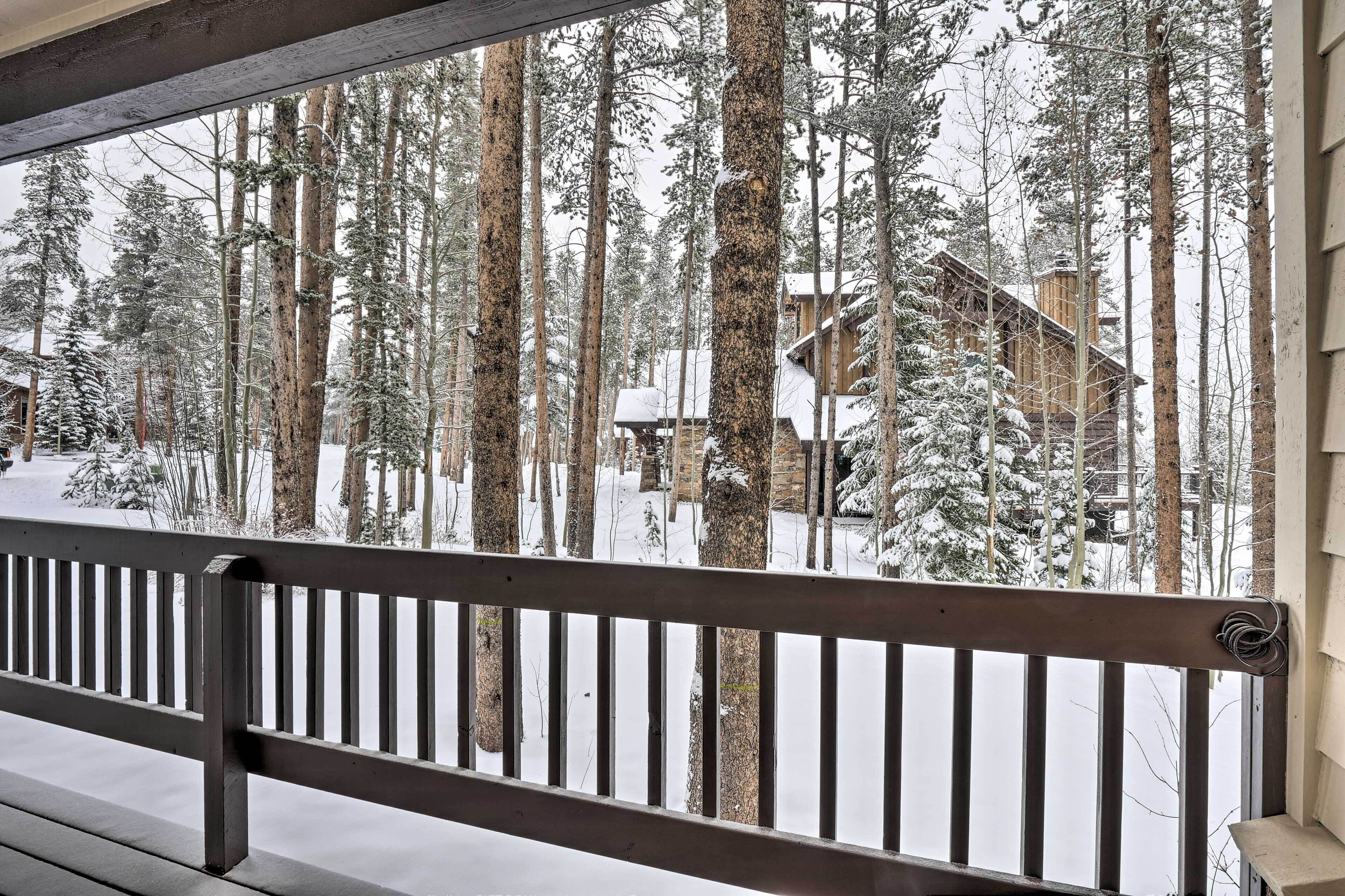 A wooden balcony railing overlooking a snowy forest with a cabin.