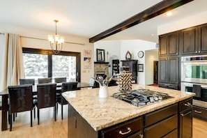 A modern kitchen with dark wood cabinets, a granite countertop, and a gas stove. - Hot Tub & Ski Shuttle: Forested Breckenridge Home! (Breckenridge)