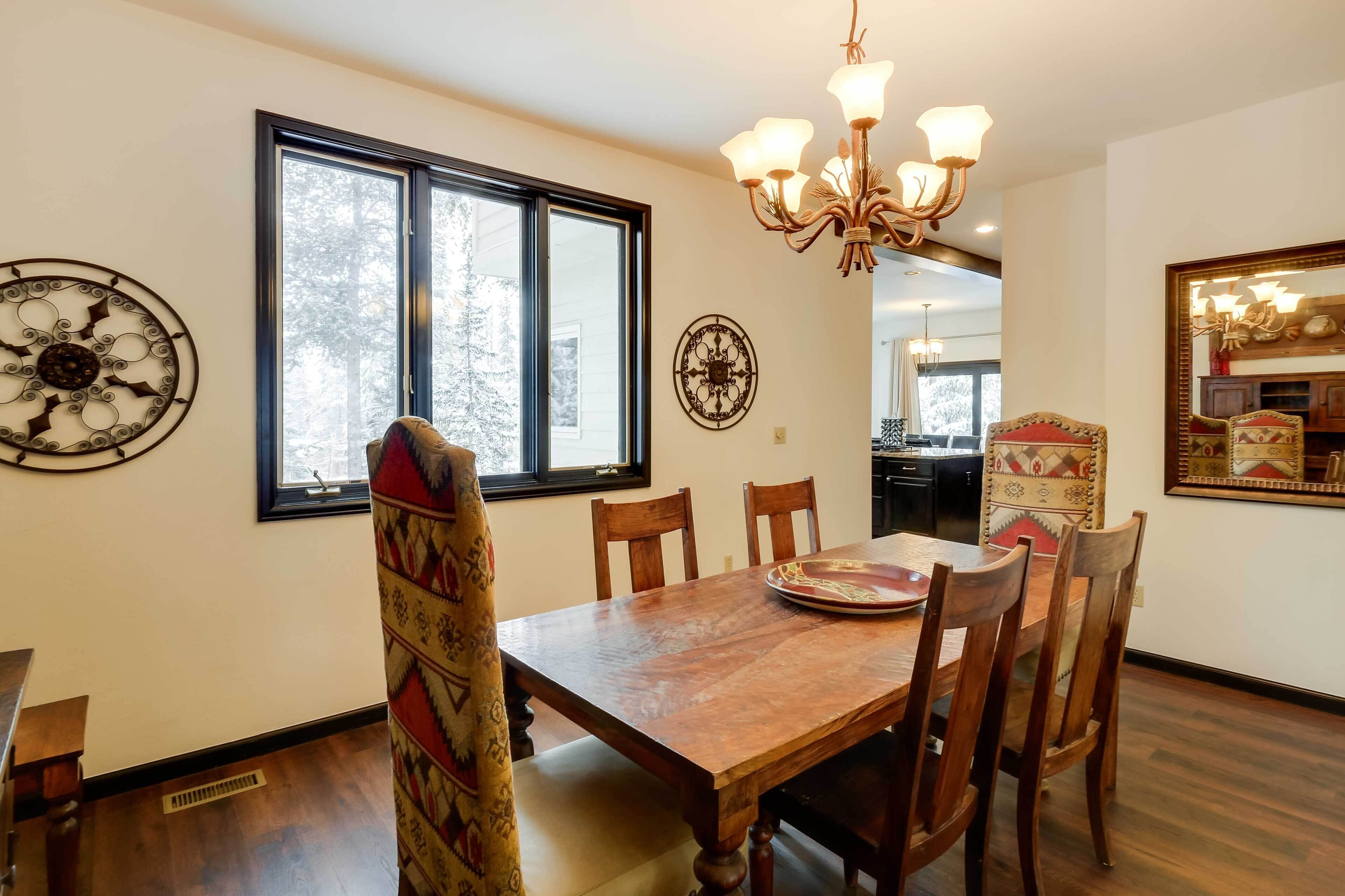 A dining room with a wooden table, four chairs, a chandelier, and decorative wall art.