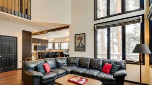 A spacious living room with a leather sectional sofa, a coffee table, and a large window offering a view of the outdoors. - Hot Tub & Ski Shuttle: Forested Breckenridge Home! (Breckenridge)