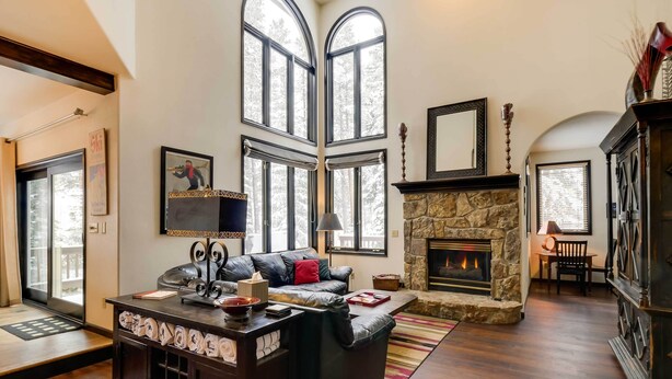 A spacious living room with a stone fireplace, leather sofa, and large windows. - Hot Tub & Ski Shuttle: Forested Breckenridge Home! (Breckenridge)