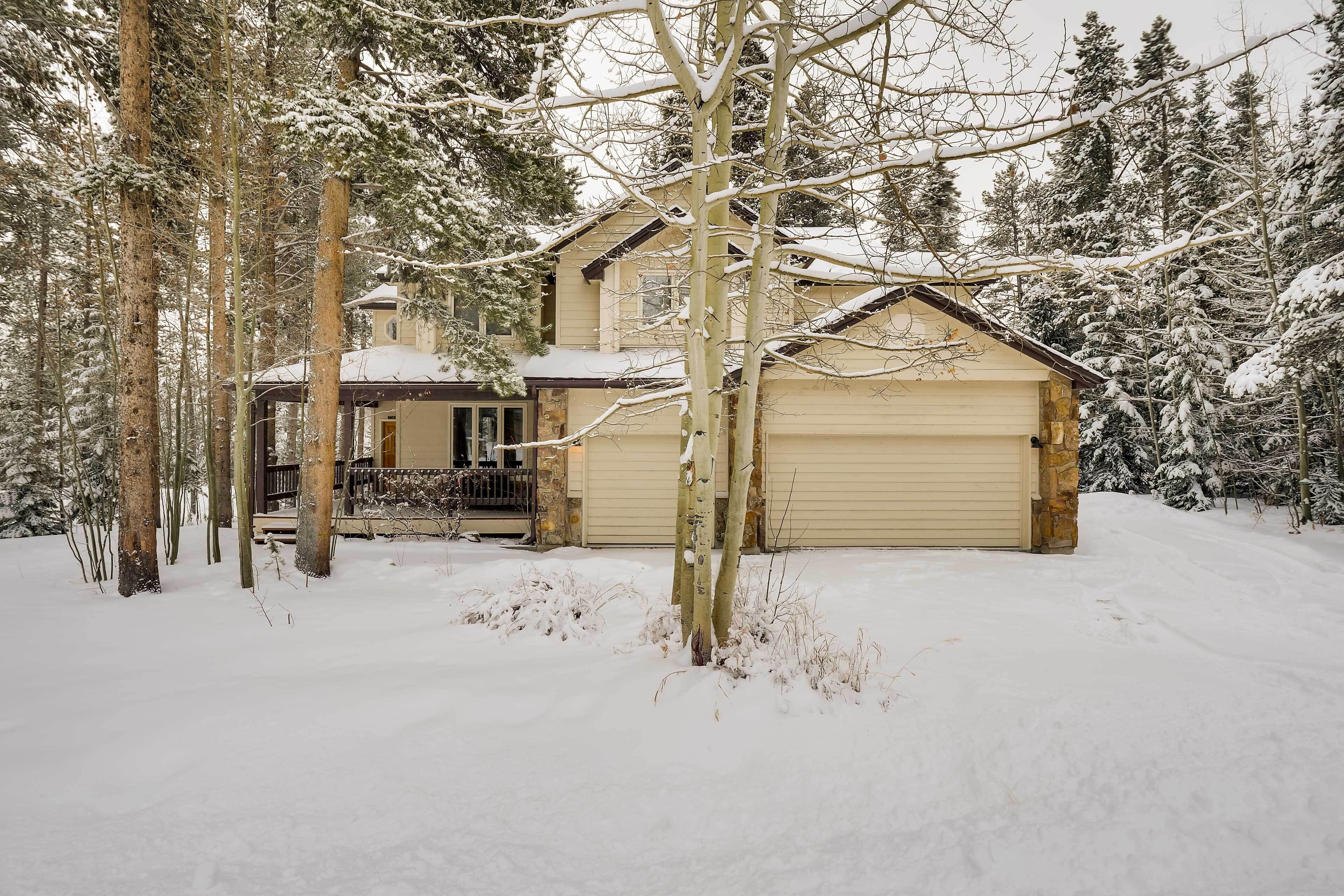 Een huis met twee verdiepingen en een garage, omgeven door met sneeuw bedekte bomen.
