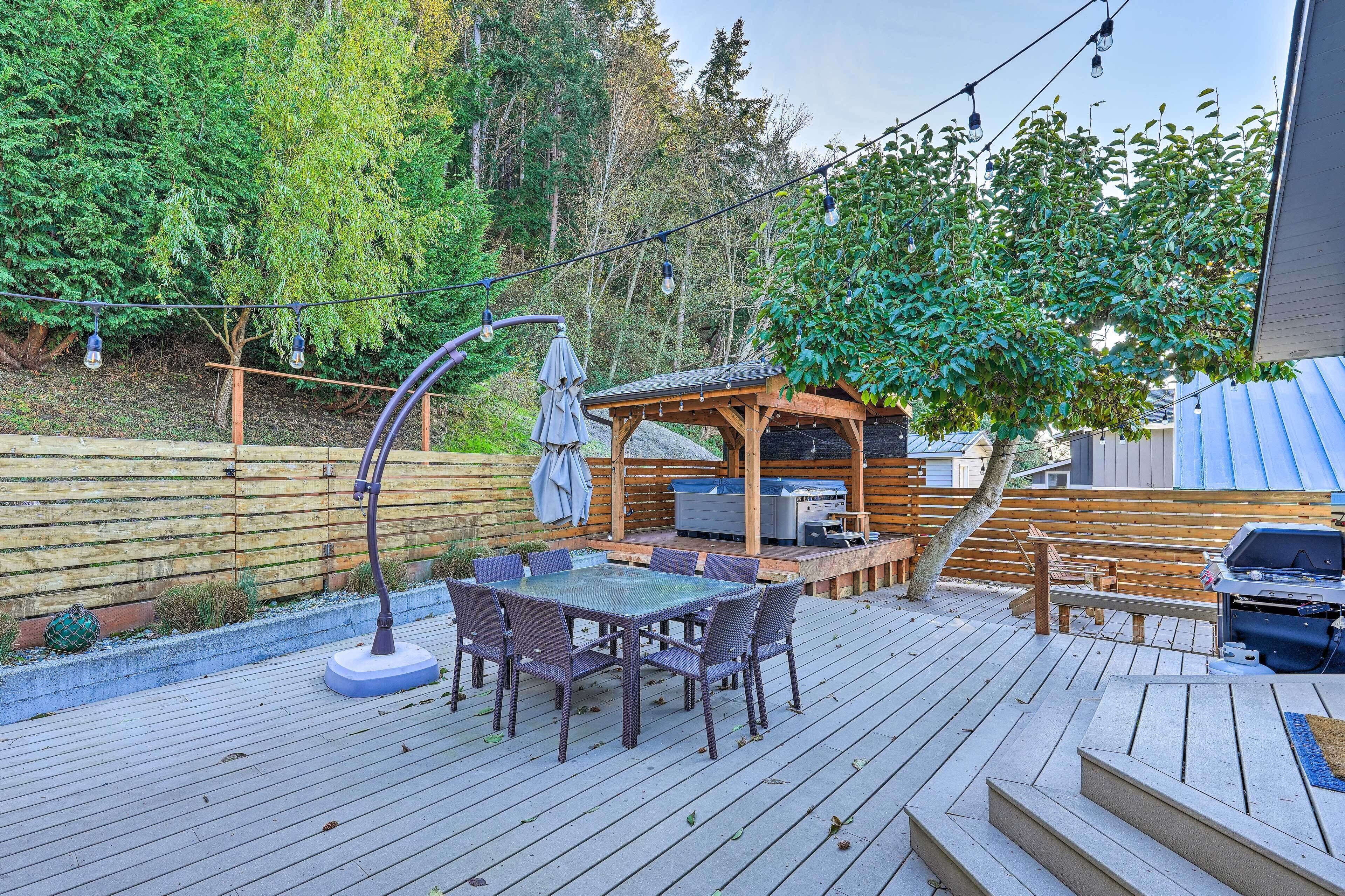 A wooden deck with a glass-top table and chairs, a barbecue grill, and a pergola with string lights.