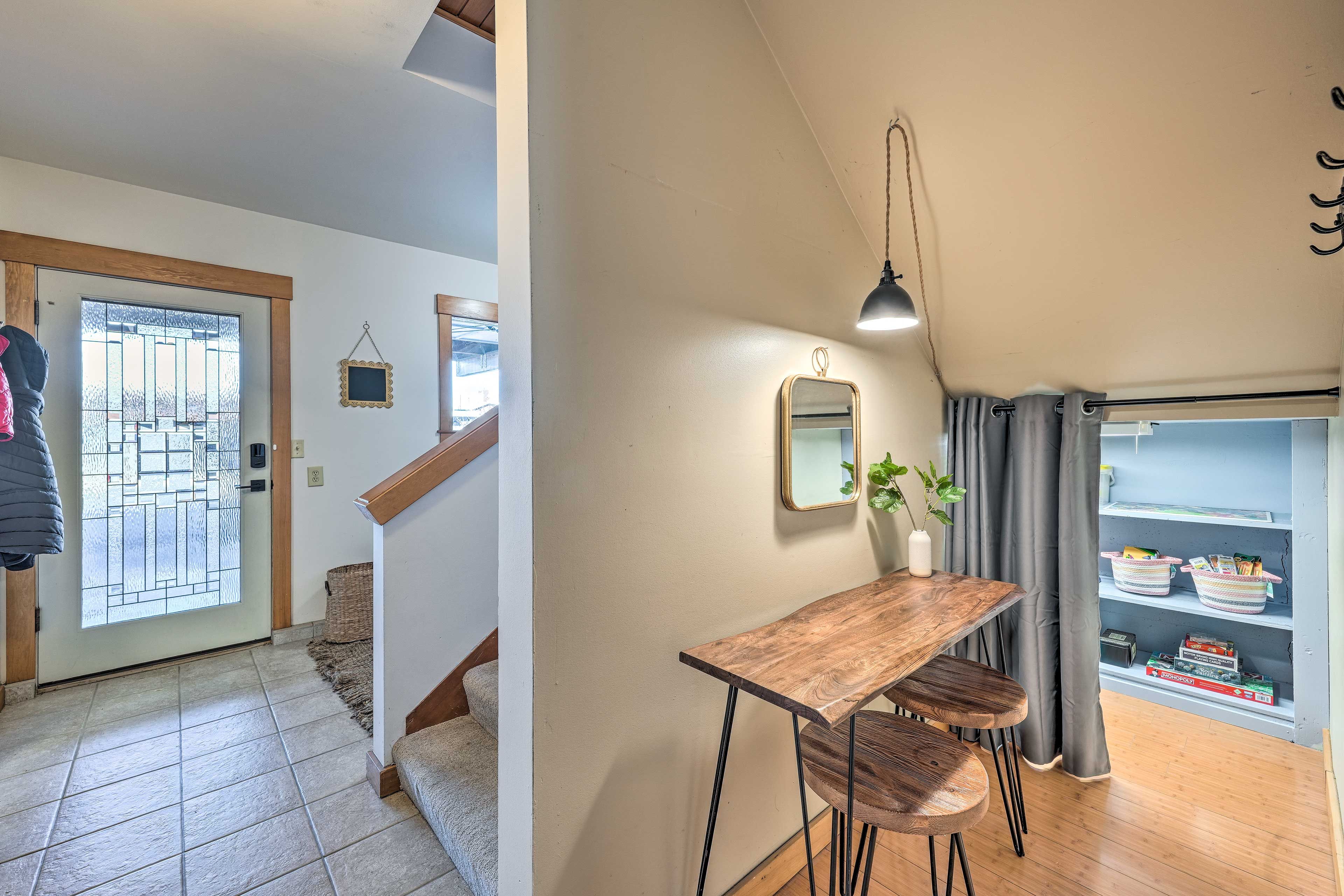 A hallway with a wooden table and chairs, a hanging lamp, and a shelf with items.