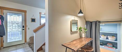 A hallway with a wooden table and chairs, a hanging lamp, and a shelf with items.