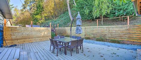 Una terraza de madera con una mesa y sillas de superficie de vidrio, rodeada por una valla de madera y árboles.