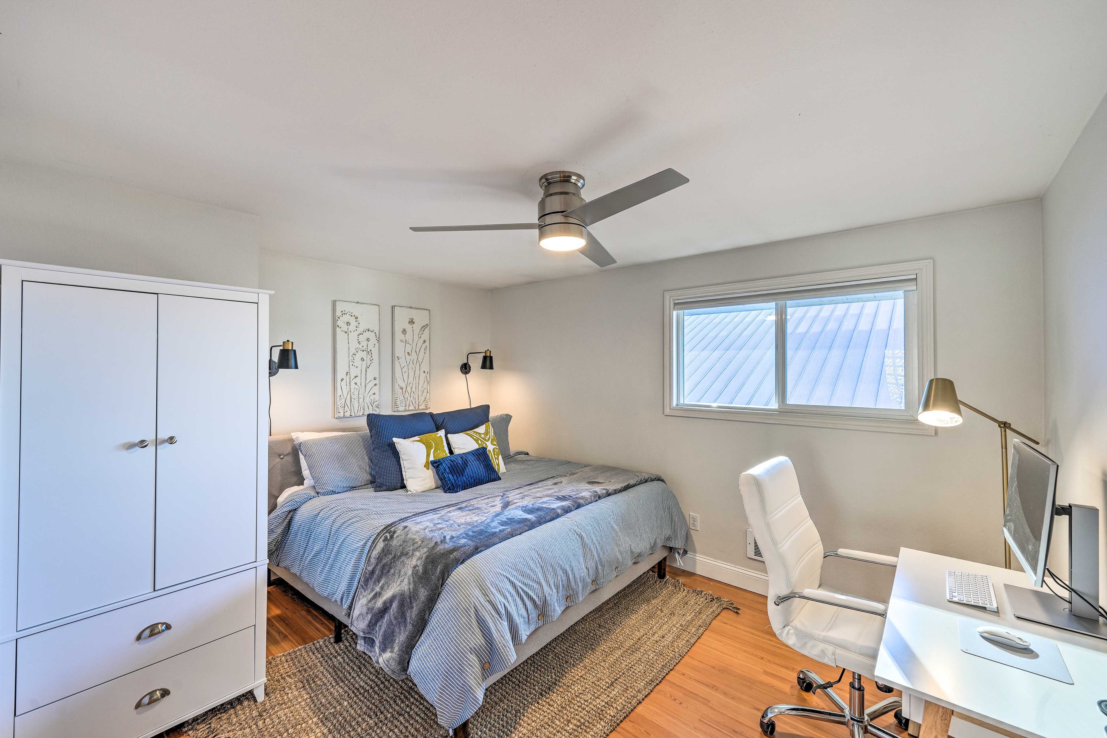 Une chambre à coucher comprenant un lit, un bureau, une chaise, une armoire, un ventilateur de plafond et une fenêtre.