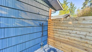 A wooden deck with a blue metal siding house, a wooden fence, and a blue hose on the ground. - Mckees Beach House w/ Ocean Views, Hot Tub! (Stanwood)